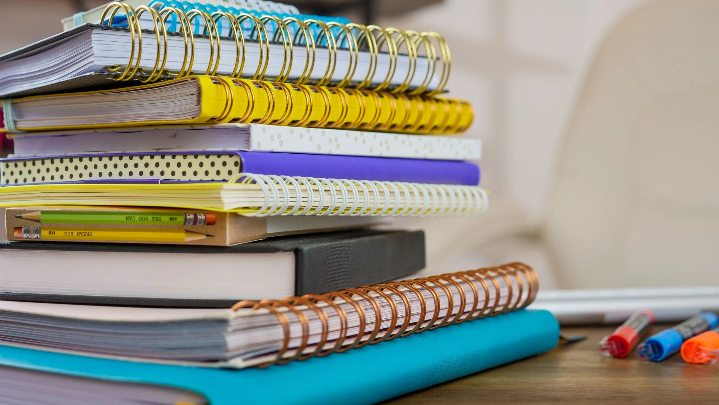 A stack of books and spiral notebooks with pencils on a desk.